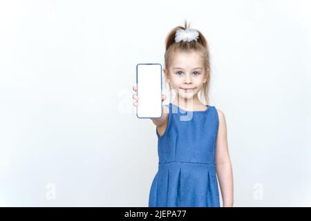 Kleines Kind Mädchen 6 Jahre alt in legerer Kleidung halten Handy mit leerem Bildschirm Arbeitsplatz auf grauem Hintergrund . Lifestyle-Konzept für die Kindheit. Stockfoto