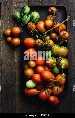 Frische rote und grüne Tomaten in einem Tablett auf Holzboden. Stockfoto