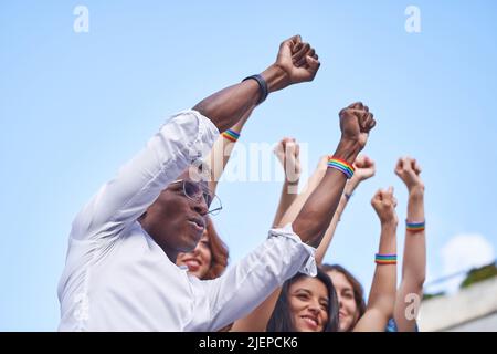 Gruppe von Menschen mit mehreren Rassen, die mit LGBT-Armbändern mit Regenbogenflagge im Freien Fäuste erheben. Konzept von Vielfalt, Gleichheit und Einheit. Stockfoto