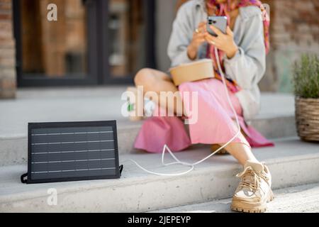 Frau Laden Telefon von einem tragbaren Solarpanel Stockfoto