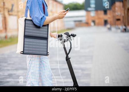 Stilvoller Kerl fährt Elektroroller und nutzt Handy unterwegs Stockfoto