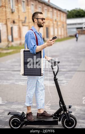 Stilvoller Kerl fährt Elektroroller und nutzt Handy unterwegs Stockfoto