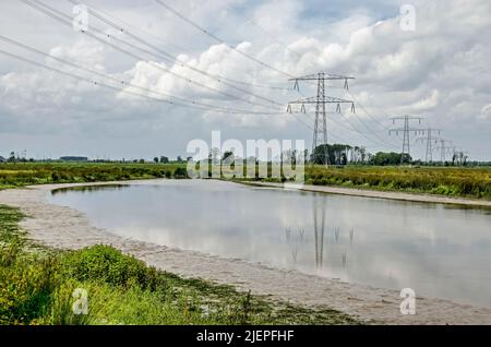 Strommasten und Stromleitungen spiegeln sich an einem Sommertag in der Region Noordwaard im Nationalpark Biesbosch in einem Gewässer mit schlammigen Bänken wider Stockfoto