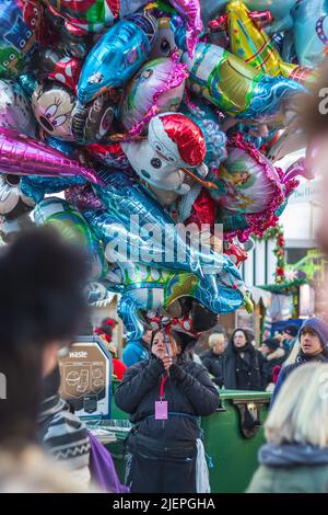 London, Großbritannien - 2. Dezember 2021 - die Verkäuferin der Straße verkauft mehrere Heliumballons mit Comicfiguren im Weihnachtsmarkt im Winterwunderland Stockfoto