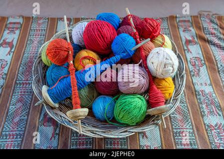 Draufsicht auf einen Korb mit Alpaka-Wollgarnkugeln und Spinnspindeln in einem Textilproduktionszentrum in Cusco, Peru. Stockfoto