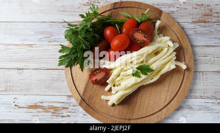 Streichkäse oder Käsepeitsche - salziger Snack-Käse mit Kirschtomaten und Kräutern auf Schneidebrett. Türkischer Käse Stockfoto