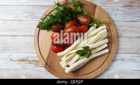 Streichkäse oder Käsepeitsche - salziger Snack-Käse mit Kirschtomaten und Kräutern auf Schneidebrett. Türkischer Käse Stockfoto