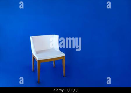 Weißer Stuhl mit Holzbeinen auf blauem Hintergrund. Stockfoto