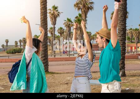 Freunde feiern den Beginn der Sommerzeit am Strand. Multirassische Gruppe von Teenagern mit erhobenen Armen. Die Schule ist vorbei. Stockfoto