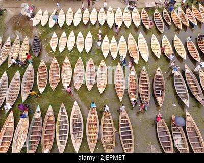 Manikganj, Dhaka, Bangladesch. 28.. Juni 2022. Hunderte von handgefertigten Holzbooten stehen auf dem größten Bootsmarkt von Bangladesch in Manikgonj, Bangladesch, zum Verkauf. Die Menschen strömten auf den Freiluftmarkt, um Boote zu kaufen, um sich auf die kommende Regenzeit vorzubereiten. Bangladesch, bekannt als „Ground Zero for Climate change“, ist mit zusätzlichem Stress konfrontiert, da fast 75 % von Bangladesch unter dem Meeresspiegel liegen und jährlich mit Überschwemmungen konfrontiert sind. Wird von den Einheimischen während des Monsuns verwendet, wenn starke Regenfälle das Flussufer zum Platzen bringen und nahe gelegene Städte und Dörfer untertauchen, kostet jedes Schiff zwischen Â£30 und Â£80 je nach Bedarf Stockfoto