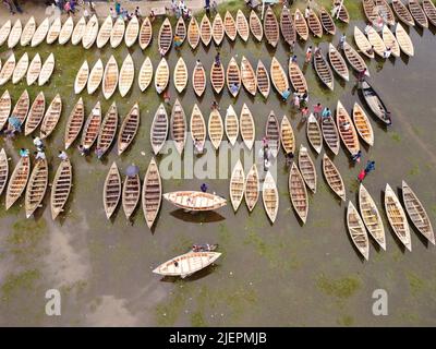 Manikganj, Dhaka, Bangladesch. 28.. Juni 2022. Hunderte von handgefertigten Holzbooten stehen auf dem größten Bootsmarkt von Bangladesch in Manikgonj, Bangladesch, zum Verkauf. Die Menschen strömten auf den Freiluftmarkt, um Boote zu kaufen, um sich auf die kommende Regenzeit vorzubereiten. Bangladesch, bekannt als „Ground Zero for Climate change“, ist mit zusätzlichem Stress konfrontiert, da fast 75 % von Bangladesch unter dem Meeresspiegel liegen und jährlich mit Überschwemmungen konfrontiert sind. Wird von den Einheimischen während des Monsuns verwendet, wenn starke Regenfälle das Flussufer zum Platzen bringen und nahe gelegene Städte und Dörfer untertauchen, kostet jedes Schiff zwischen Â£30 und Â£80 je nach Bedarf Stockfoto