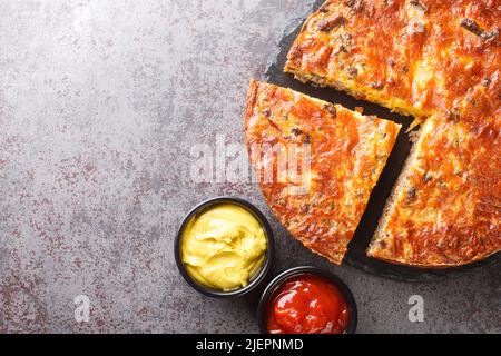 Köstliche, beliebte Fleisch-Cheeseburger-Pie mit Saucen aus der Nähe auf einem Schieferbrett auf dem Tisch serviert. Horizontale Draufsicht von oben Stockfoto