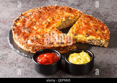 Hausgemachter knuspriger Cheeseburger-Kuchen mit Saucen aus der Nähe auf einem Schieferbrett auf dem Tisch serviert. Horizontal Stockfoto