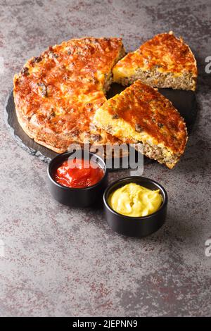 Pikante Cheeseburger Pie im Südstaaten-Stil mit Hackfleisch-Cheddar-Käse und Zwiebeln in Nahaufnahme auf einem Schieferbrett auf dem Tisch. Vertikal Stockfoto