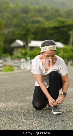 Eine Dame mittleren Alters in Sportbekleidung schnürt vor dem Laufen Schnürsenkel und macht sich bereit für das Joggen im Freien. Gesundes Lifestyle-, Workout- und Wellness-Konzept Stockfoto