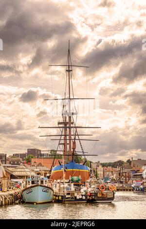 Eine Nachbildung des Hochschiffs HMS Endeavour, das im Hafen festgemacht wurde. Fischerboote stehen vor dem Hotel und ein wolkiger Himmel ist oben. Stockfoto