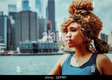 Headshot schöne junge Erwachsene Frau Afro Frisur mit Manhattan New York City Skyline im Hintergrund Außenaufnahme Stockfoto