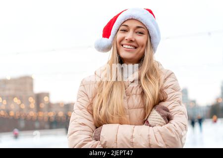 Outdoor-Porträt junge schöne modische Frau trägt Santa Hut, posiert Straße der europäischen Stadt. Winter Weihnachtsferien Konzept. Schlittschuhlaufen Stockfoto
