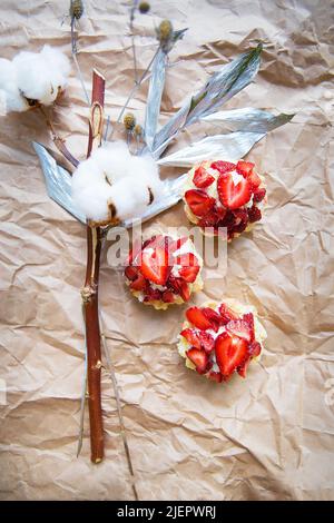 Schöne kleine Kuchen mit Erdbeeren zusammen mit einem Zweig auf Kraftpapier. Stockfoto