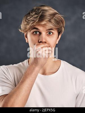 Junger verängstigte Mann im T-Shirt auf grauem Hintergrund. Stockfoto
