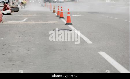 Arbeiter reparieren die Straße. Leuchtend orange Verkehrskegel stehen in einer Reihe auf Asphalt Stockfoto