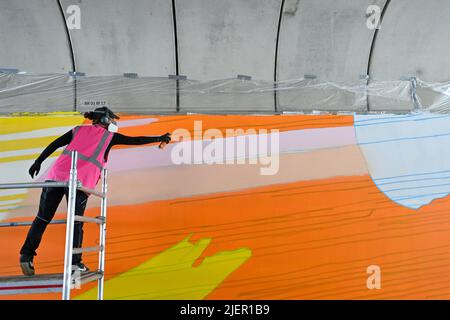 Magdeburg, Deutschland. 28.. Juni 2022. Die Künstlerin Claudia Walde sprüht ihr Graffito auf die Betonwand des Brückenlagers in einer Bahnüberführung am Hauptbahnhof. Es ist eines von zwei Graffiti von je 250 Quadratmetern des Künstlers, das die Wiederlagerung in Zukunft schmücken wird. Die Arbeiten sollten bis Ende der Woche abgeschlossen sein. Aus rund 300 Dosen wird dann Farbe auf den Beton gesprüht. Quelle: Klaus-Dietmar Gabbert/dpa/Alamy Live News Stockfoto