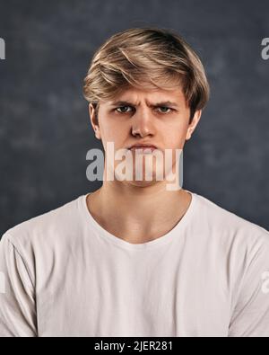 Verärgert junger Mann in T-Shirt auf grauem Hintergrund. Stockfoto