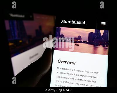Person, die Smartphone mit der Website der Bahrain Mumtalakat Holding Company auf dem Bildschirm vor dem Logo hält. Konzentrieren Sie sich auf die Mitte des Telefondisplays. Stockfoto