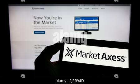 Person mit Mobiltelefon und Logo des US-Finanzunternehmens MarketAxess Holdings Inc. Auf dem Bildschirm vor der Webseite. Konzentrieren Sie sich auf die Telefonanzeige. Stockfoto