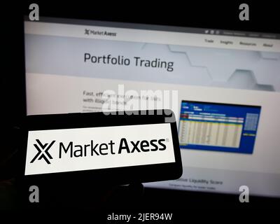 Person, die Mobiltelefon mit dem Logo des amerikanischen Finanzunternehmens MarketAxess Holdings Inc. Auf dem Bildschirm vor der Webseite hält. Konzentrieren Sie sich auf die Telefonanzeige. Stockfoto