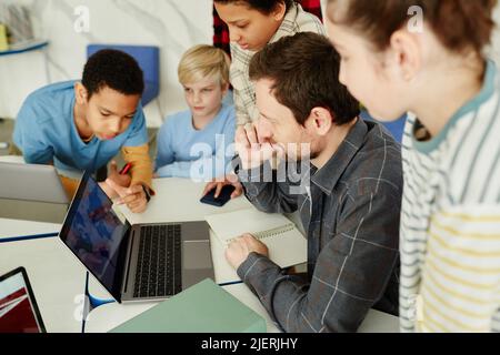 Hochwinkelporträt eines männlichen Lehrers mit einer Gruppe von Kindern, die in der Schule einen Laptop benutzen Stockfoto