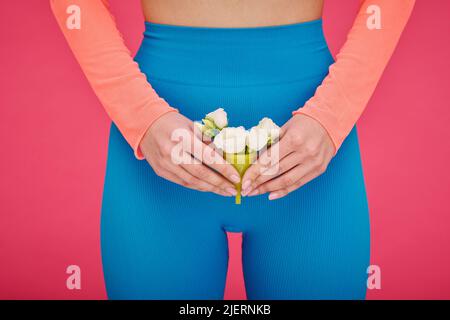 Nahaufnahme einer jungen Frau, die Menstruationstasse mit weißen Blüten im Inneren auf rosa Hintergrund isoliert hält Stockfoto