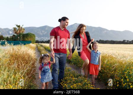 Glückliche Familie Vater der Mutter und zwei Töchter Schwestern zu Fuß auf dem Land Natur bei Sonnenuntergang.sorglose Eltern Spaß mit ihren Kindern auf einem Feld. Stockfoto