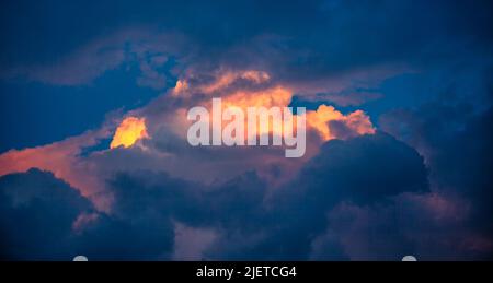 Orangefarbene Wolken in der Mitte des Dunkelblauen, beleuchtet von der Sonne bei Sonnenuntergang. Abstrakter Himmel bei Sonnenuntergang Stockfoto