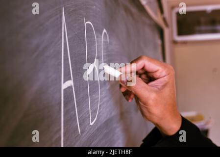 Eine Hand eines Lehrers, der das ABC-Alphabet mit Kreide in einer Englischstunde auf die Tafel schreibt. Stockfoto