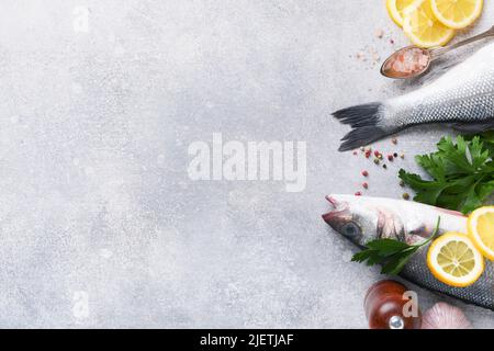 Frischer Fisch. Seebarsch roh mit Salz, Pfeffer, Petersilie, Olivenöl und Zitrone auf Schneidebrett auf hellgrauem Beton rustikalen Hintergrund. Essen Kochen Backg Stockfoto