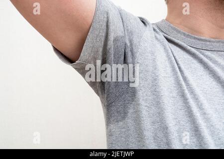 Verschwitzte Achselhöhlen, nasser Achselfleck auf grauem T-Shirt Stockfoto