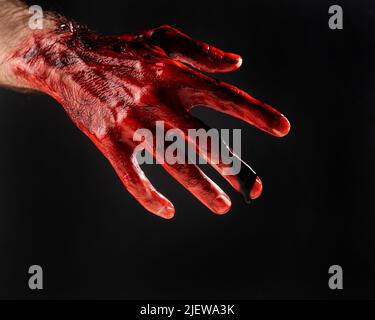 Nahaufnahme einer mit Blut befleckten männlichen Hand auf schwarzem Hintergrund. Stockfoto