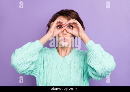 Foto-Portrait lustige Mädchen halten Hände wie binokular starren in gestrickten Pullover isoliert auf pastellvioletten Hintergrund Stockfoto