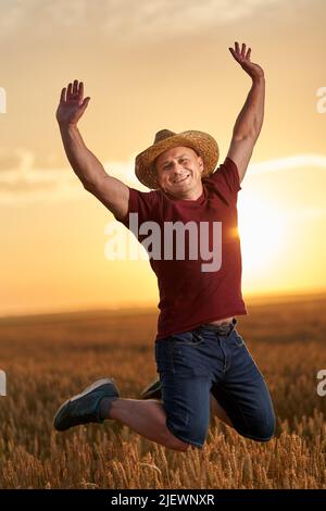 Bauer springt vor Freude in seinem Weizenfeld bei Sonnenuntergang Stockfoto