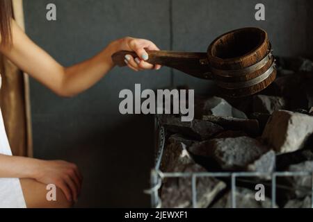 Nahaufnahme der Frau, die in der Sauna Wasser in heißen Stein gießt Stockfoto