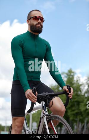 Mann in Sonnenbrillen rast vor dem Hintergrund des Sommerparks entlang der Straße. Mann mit Fahrrad-Hobby fährt im Park. Stockfoto