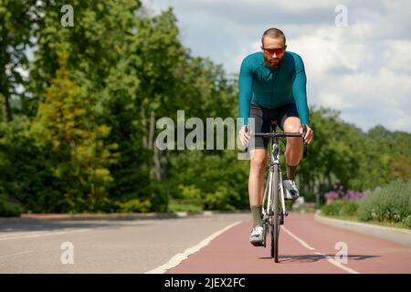 Porträt eines sportlichen Mannes in einem Radsport-Outfit, der mit einem Fahrrad auf der Bike Lane steht und für die Kamera posiert Stockfoto