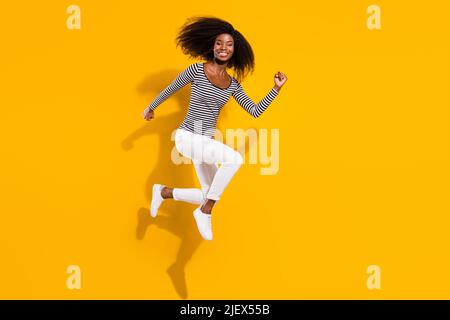 In voller Länge Körpergröße Foto Frau springen hoch läuft zum Verkauf in gestreiftem Hemd isoliert leuchtend gelbe Farbe Hintergrund Stockfoto