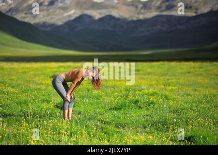 Seitenansicht Porträt eines erschöpften Läufers, der auf einem Feld in einem hohen Berg ruht Stockfoto