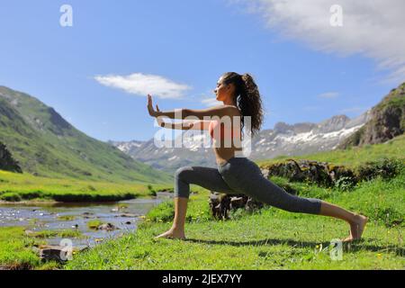 Seitenansicht Porträt einer Frau, die auf dem grünen hohen Berg neben einem Fluss Tai Chi praktiziert Stockfoto