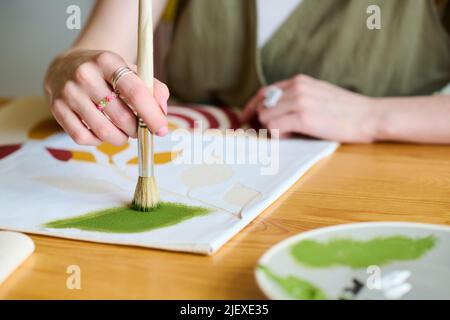 Hand der jungen kreativen Künstlerin mit Pinsel setzen grüne Aquarell auf Papier, während die Schaffung neuer abstrakter Malerei Stockfoto