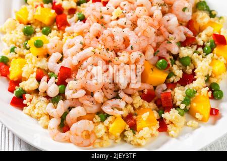 Gekochte kleine rosafarbene Garnelen auf Hirsebrei mit Gemüse, Mangostückchen auf weißem Teller auf weißem Tisch, horizontale Ansicht von oben, close-U Stockfoto