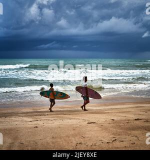 Vater und Sohn tragen ihre Surfbretter an einem Strand in Thailand Stockfoto