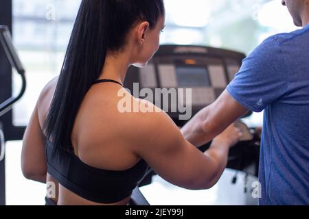 Der junge Personal Trainer hilft dem Kunden, das Laufband in der Rückansicht einzustellen Stockfoto